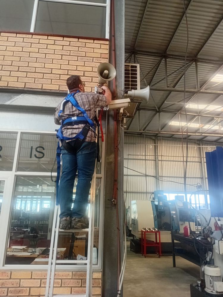 Andre installing a CCTV camera and speaker on a wall-mounted pole